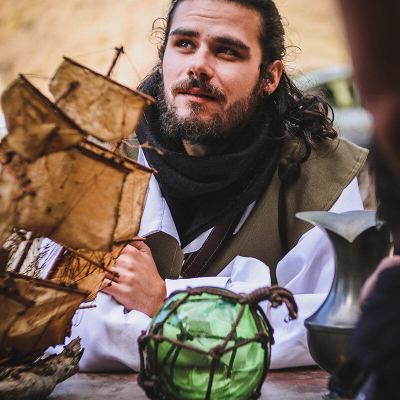 Jeune homme costumé derrière une maquette de bateau pirate