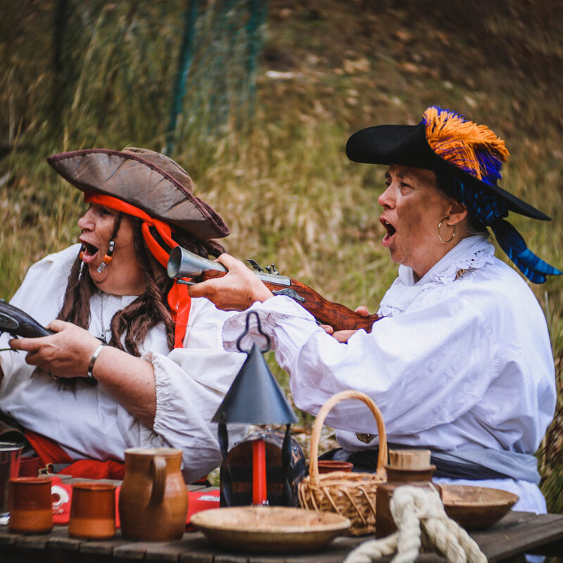 Deux femmes pirates pointent leurs armes dans la même direction en criant.